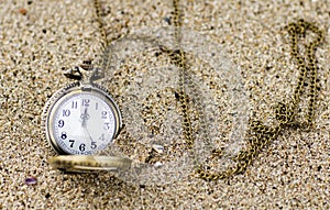 Vintage pocket watch is on the sand.