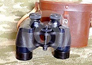 Vintage Porro prism black binoculars with case on camouflage background