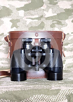 Vintage Porro prism black binoculars with case on camouflage background photo