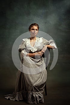 Vintage portrait of young beautiful girl in gray dress of medieval style  on dark background. Comparison of eras