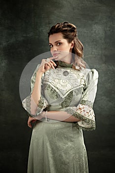 Vintage portrait of young beautiful girl in gray dress of medieval style isolated on dark background. Comparison of eras