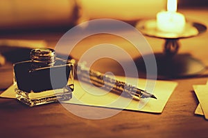 Vintage quill pen and inkwell on wooden table in candlelight