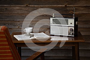 Vintage radio receiver on an old table with old-fashoned eyeglasses, book and armchair