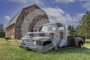 Vintage red barn with abandoned pickup truck in a farmyard on the prairies in Saskatchewan