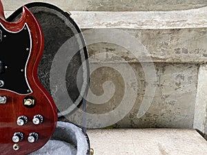 Vintage red cherry electric guitar placed in a black case with a white cement wall background. Popular models.