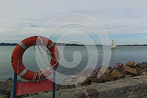 Vintage red lifebuoy on the pole in the embankment of Balaton lake. Vibrant sky in cloudy day. Beautiful autumn landscape