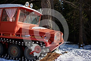 Vintage red tracked snow vehicle parked by trees