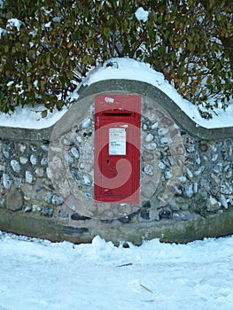 Vintage red UK post box set in stone wall in the snow