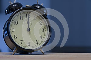 Vintage and retro analogue alarm clock indicating that it`s twelve o` clock, 12pm or 12am, on a dark blue background