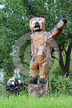 Vintage retro bear waving hello wooden sculpture next to small turtle sculpture on two cut down tree stumps surrounded with grass