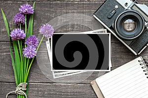 Vintage retro camera with blank photo frame, purple wildflowers and lined notebook on rustic wooden background