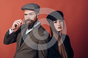 Vintage retro couple on red wall. Old style hat on bearded man and black fashion cap on beauty woman.