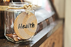 Vintage retro glass jar with hemp rope tie health tag and few coins inside on wood counter concept of save money for health care m