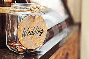 Vintage retro glass jar with hemp rope tie wedding tag and few coins inside on wood counter concept of saving money for wedding photo