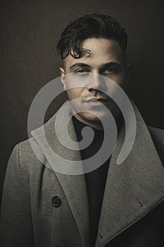 Vintage and retro portrait of illuminated man in grey coat with brown background. Young guy with old hairstyle. Fashion portrait