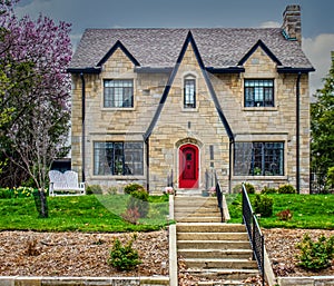 Vintage rock block house with dormers and large front paned  windows on hill with step leading up drom street in  spring