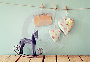 Vintage rocking horse next to fabric hearts and empty card for adding text hanging on the rope on wooden floor