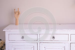 Vintage room design. Antique white cupboard, wooden mannequin hand and empty beige wall with copy space