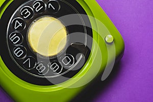 Vintage rotary phone. classic green telephone with round dial on purple background. old communication technology