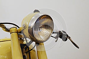 Vintage round headlight and steering handlebar on czechoslovak motorcycle from fifties of 20th century, yellow colour
