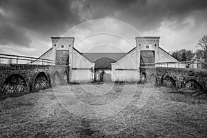 Vintage rural scene, dramatic front view of two black and white old rustic worn stone barn building farmhouse with dark sky. Two a