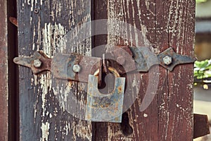 Close-up image of a vintage rusted lock on an old worn wooden fence.