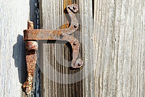 Vintage rusted metal door hinge over the weathered wooden wall.