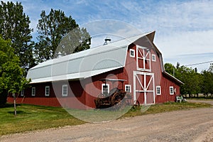 Vintage rusted tractor in front of patrimonial red wooden barn with metal gambrel roof and white trim photo