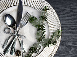 Vintage or rustic christmas table setting Elegant white plate, cutlery and natural pine tree branch on wooden surface