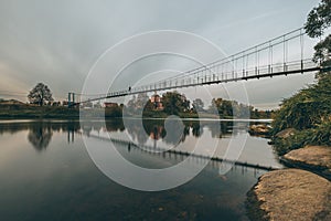 Vintage rustic suspension bridge over river in autumn. River crossing concept.