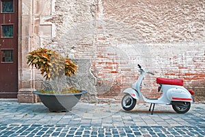 Vintage scene with a Vespa motorcicle in a small town in Italy parked in front of a church facade. Empty copy space photo
