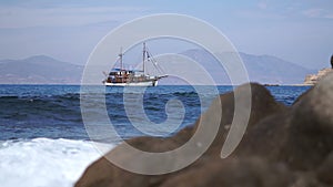 Vintage schooner anchored in the sea. Waves hit the stones in the foreground