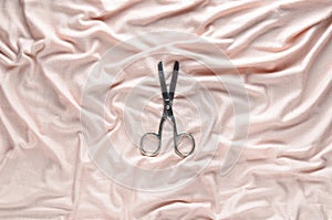 Vintage scissors on a pale pink fabric background. Top view.