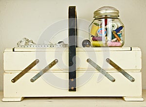A vintage sewing box, white, with some sewing thread bobbings and a measuring tape