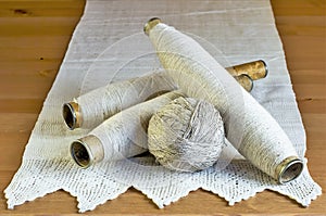 Vintage spools with natural linen threads and handmade lace tablecloth on a wooden background.