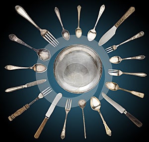 Vintage spoons, knives, forks and a plate lined with sun on a black-and-blue background.