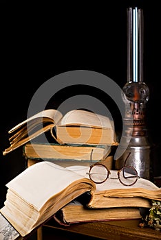Vintage still life with old spectacles on book near desk lamp. Old antique books with glasses near old paraffin lamp on the wooden