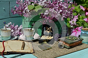 Vintage still life with open book or diary, runes, cup and lilac flowers bouquet in the garden.