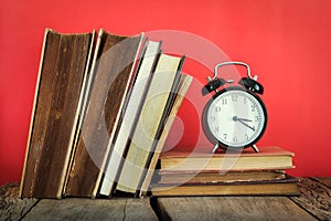 Vintage still life of stack of old books with alarm clock on red