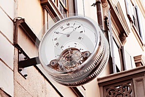 Vintage street clock with roman numerals hanging on the wall of building in center of european city. Outdoor analog