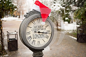 Vintage street clock with title Merry Christmas London and Santa Claus hat on them in winter park