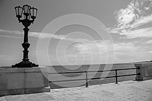 Vintage street lantern on seashore black and white. Boardwalk with street lamp monochrome. Coastline illumination.