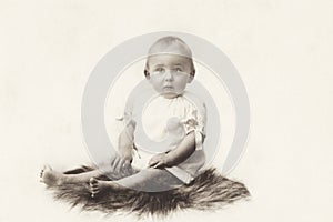 Vintage studio photograph from a  girl toddler sitting on a piece of fur, around the year 1920