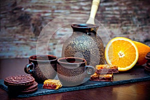 Vintage style ceramic cups, coffee brewing pot, fresh orange and chocolate cookies and candies photo