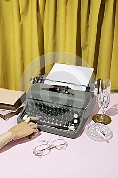 Vintage style concept with typewriter, glasses, books, wooden hand and crystal glass on yellow curtain background