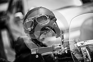 Vintage style motorbike helmet with goggles on the motorcycle handlebar. In Black and White