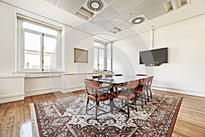 Vintage style office with rectangular wooden meeting table with wooden chairs upholstered in brown leather on a brown carpet and