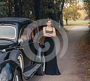 Vintage style photo. Elegant retro woman in black evening long dress posing on road, autumn nature background green