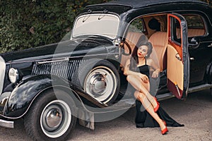 Vintage style photo. Elegant retro woman in black evening long dress posing on road, summer nature background green