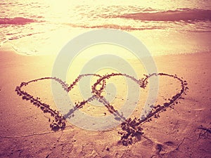Vintage style photo of two hearts shape draw on the beach.
